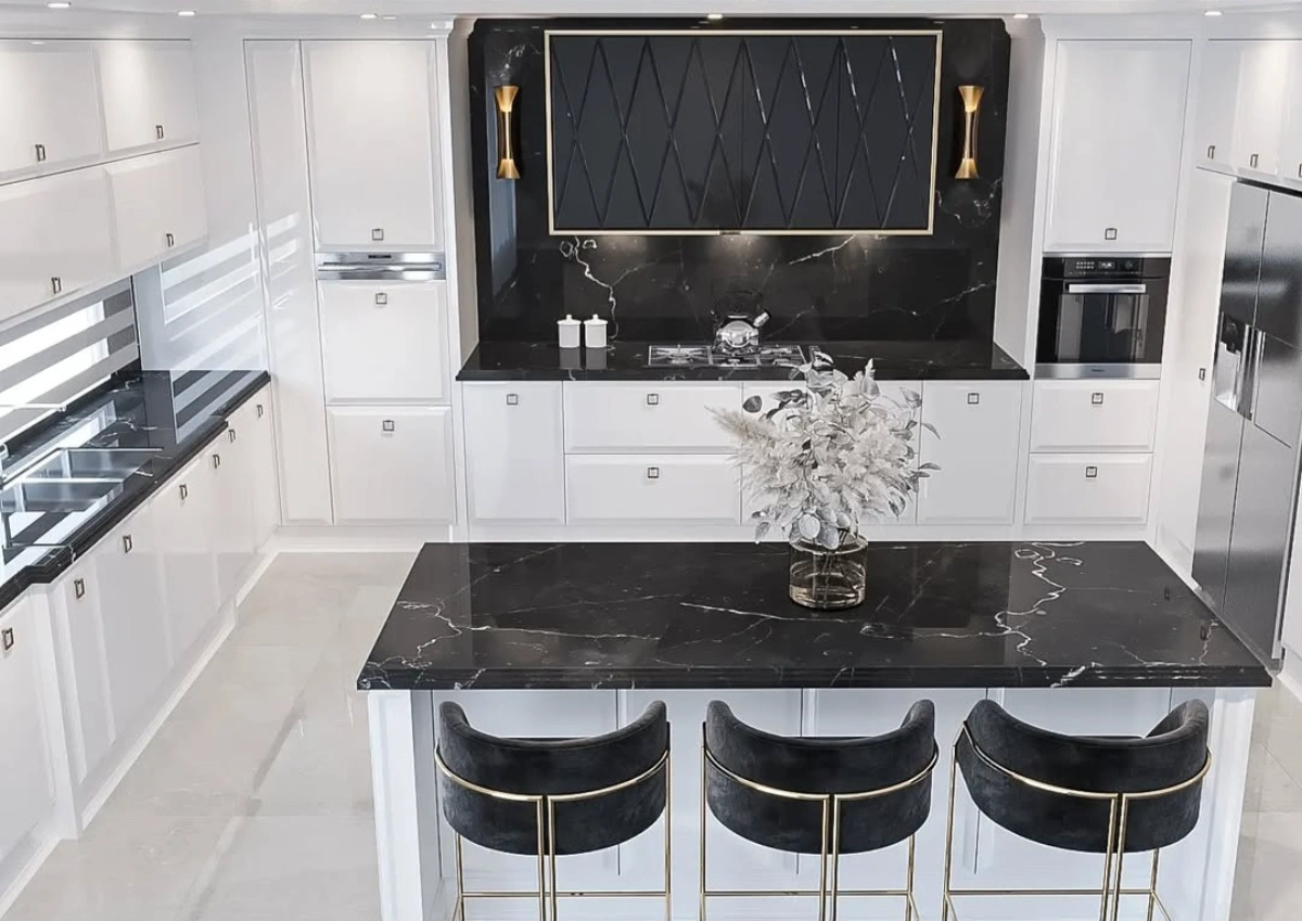 کابینت انزو سفید با کاور هود طرح‌دار مشکی و دستگیره‌های مربع نقره‌ای به همراه جزیره سفید با صفحه سنگی مشکی و رگه‌های سفید